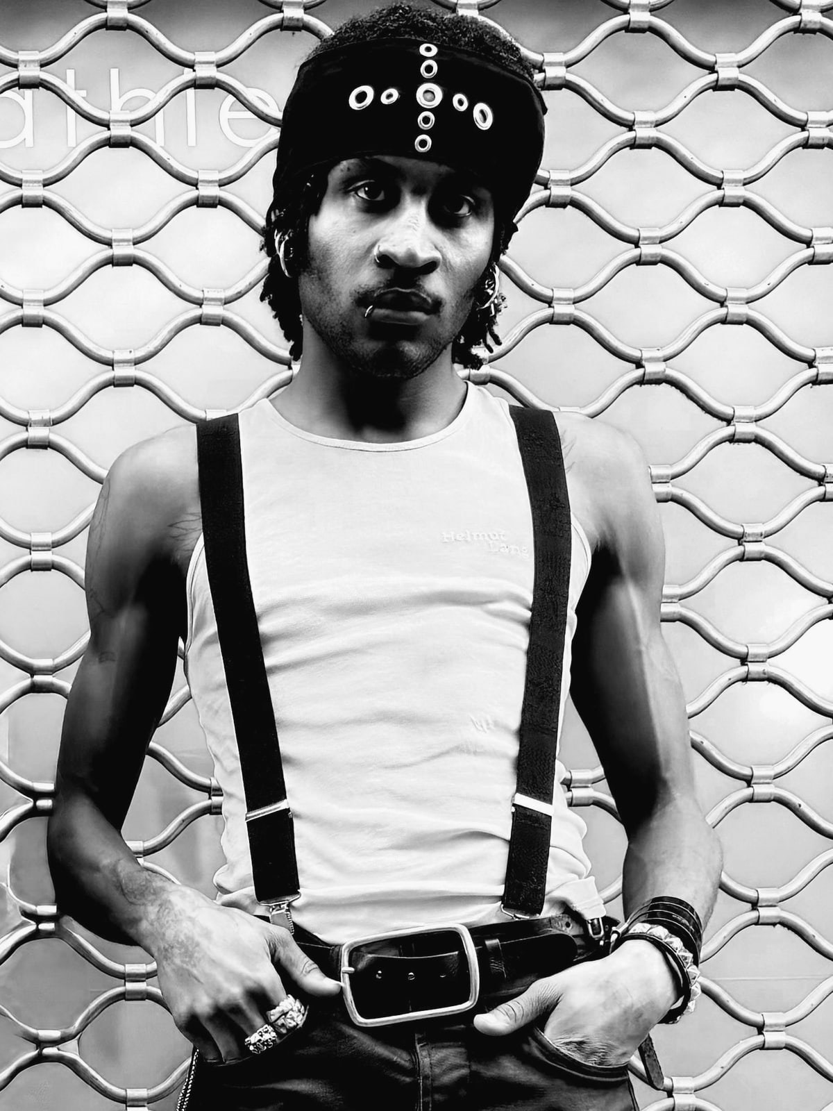 Bakary Diallo against a mesh shutter, eyelet cap, vest and suspenders, hands in his pockets