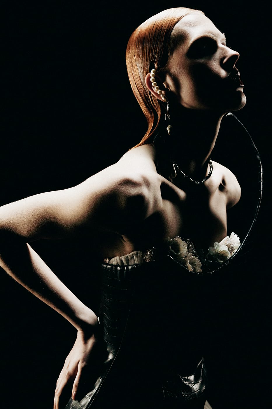 A model in a boned bodice and hooped headpiece, lit hard against black