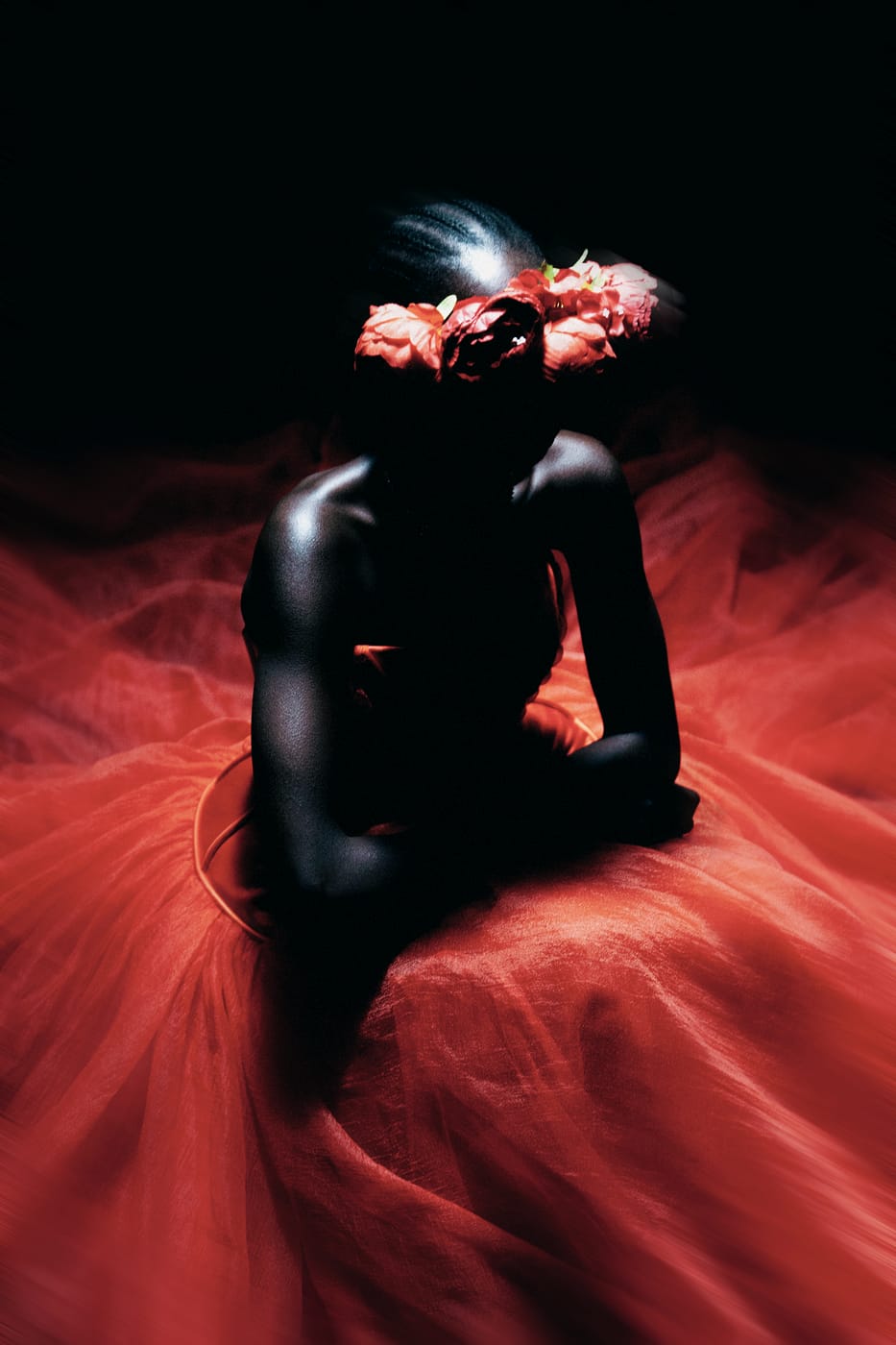 A model seated in a bank of red tulle, flowers at the head