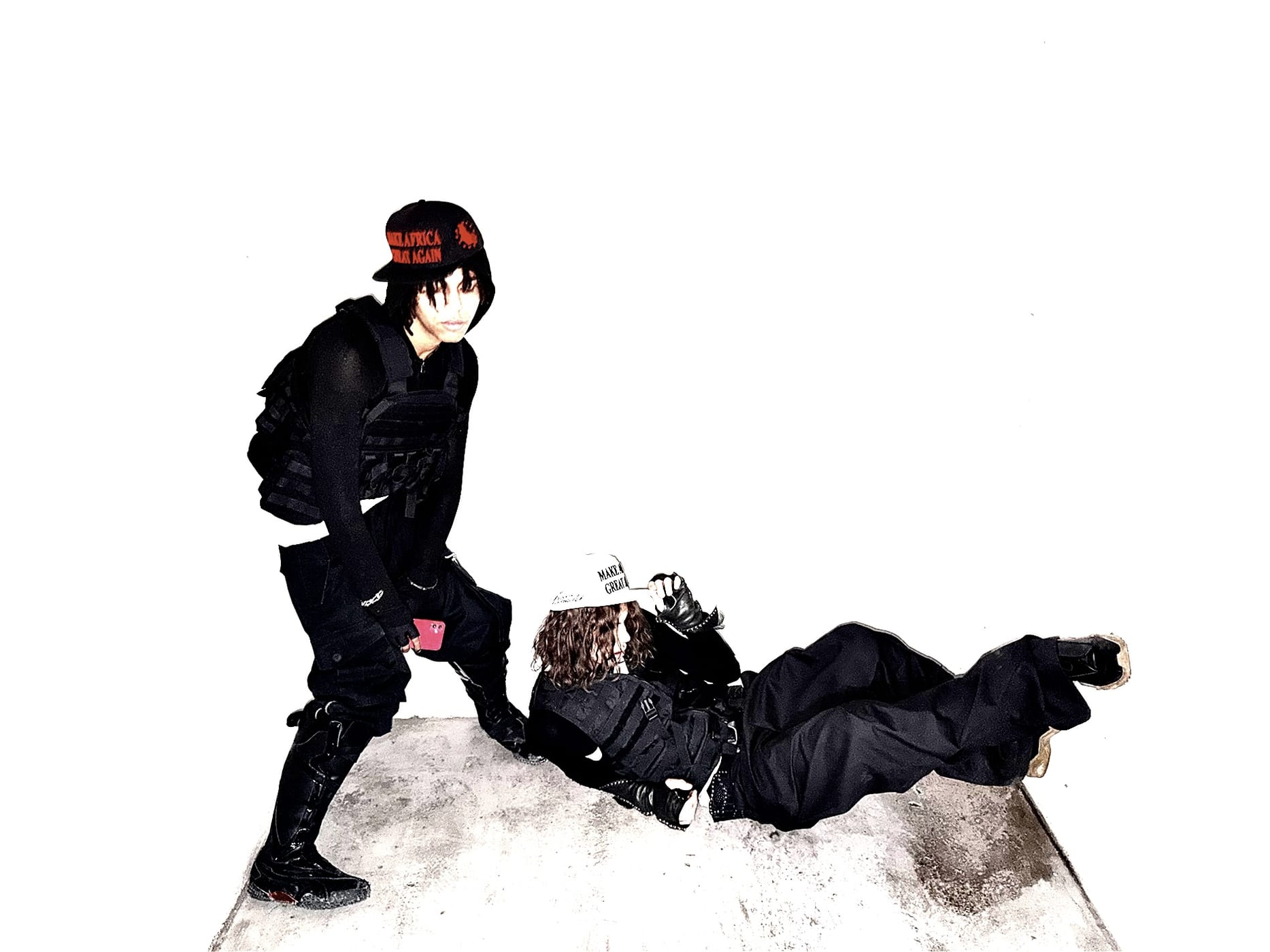 Two figures in tactical black and the cap, one standing over the other on a white ground