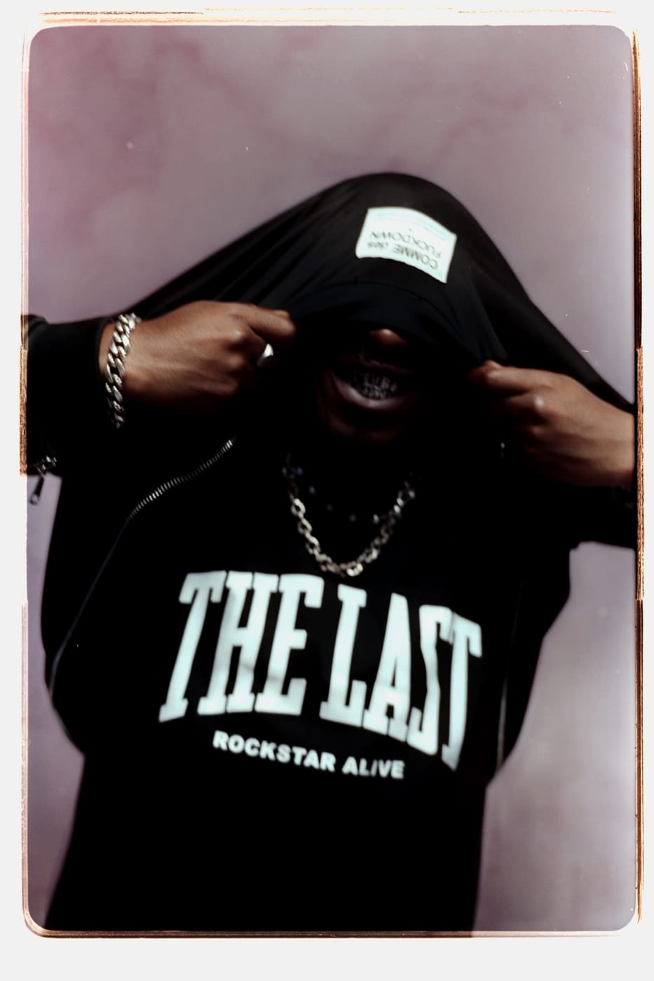Peso Shabba pulling a labelled jacket up over his head, chain and grill showing