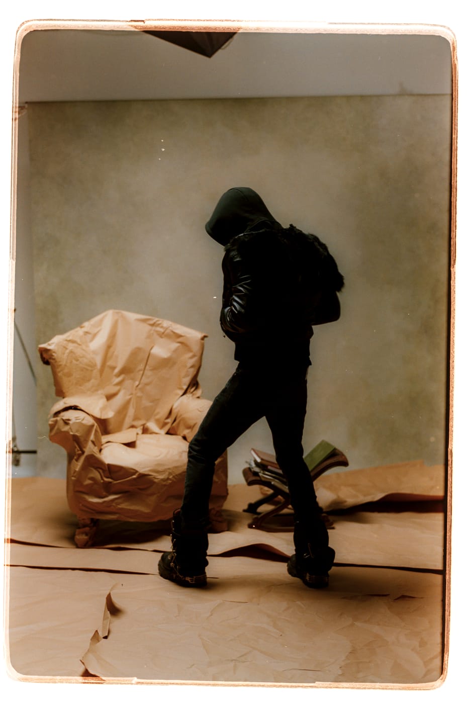 Peso Shabba hooded and turned away, a paper-wrapped armchair beside him