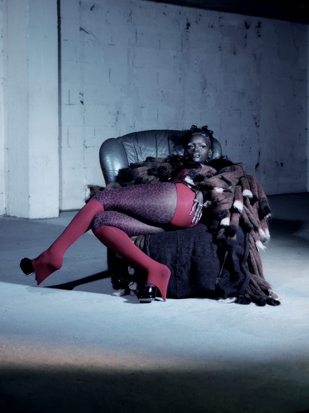 Ezek sunk into a leather armchair under a patchwork fur, red tights, legs crossed in blue light