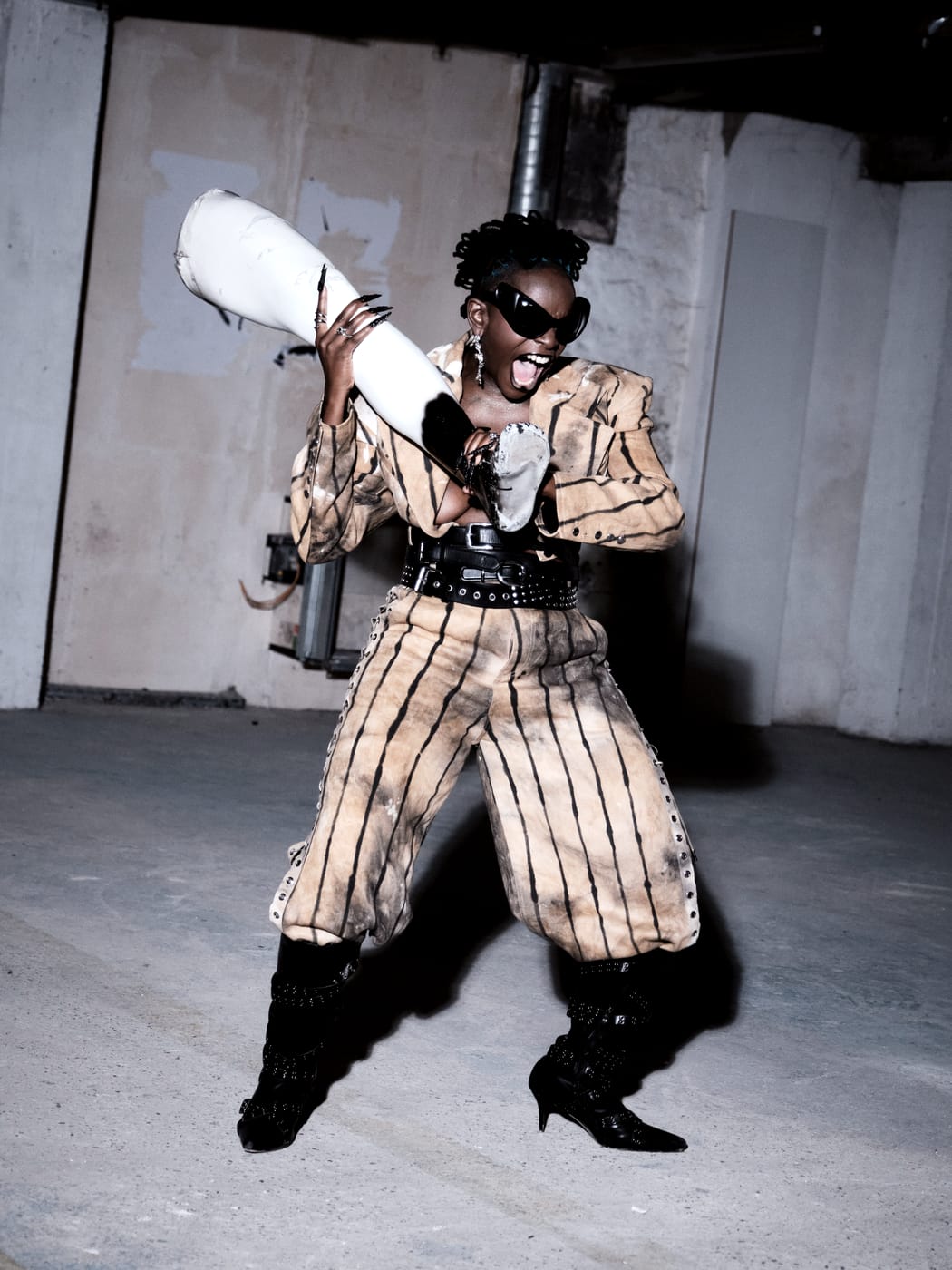 Ezek laughing with a length of white pipe over her shoulder, striped suit and sunglasses