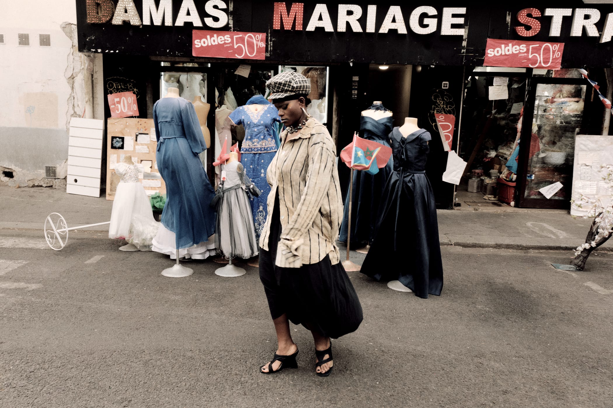 Ezek crossing the street past a wedding-dress shopfront, beret and black skirt