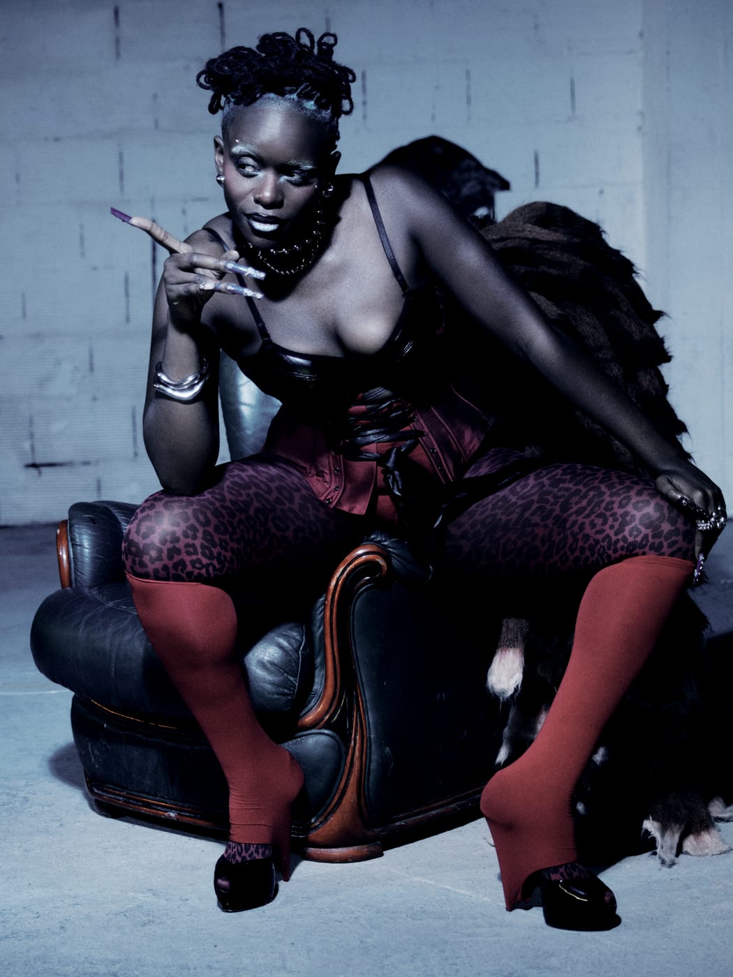 Ezek seated on the armchair's arms, red socks planted, a hand raised mid-word