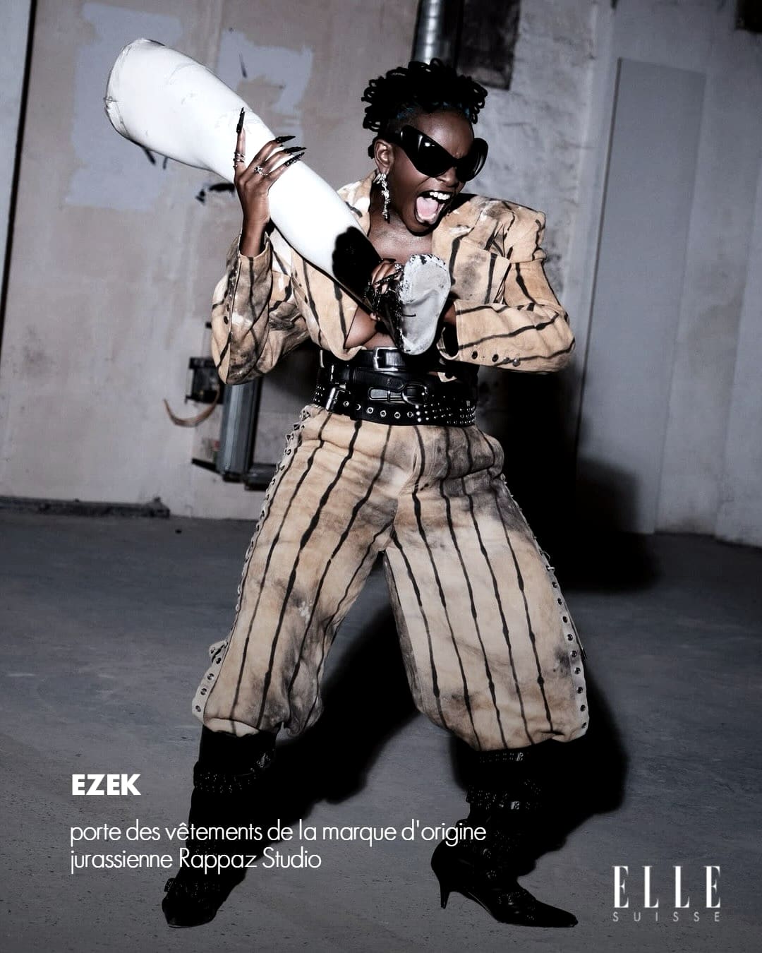 ELLE Suisse card: Ezek shouting in a striped suit, a length of white pipe over her shoulder, dressed by Rappaz Studio