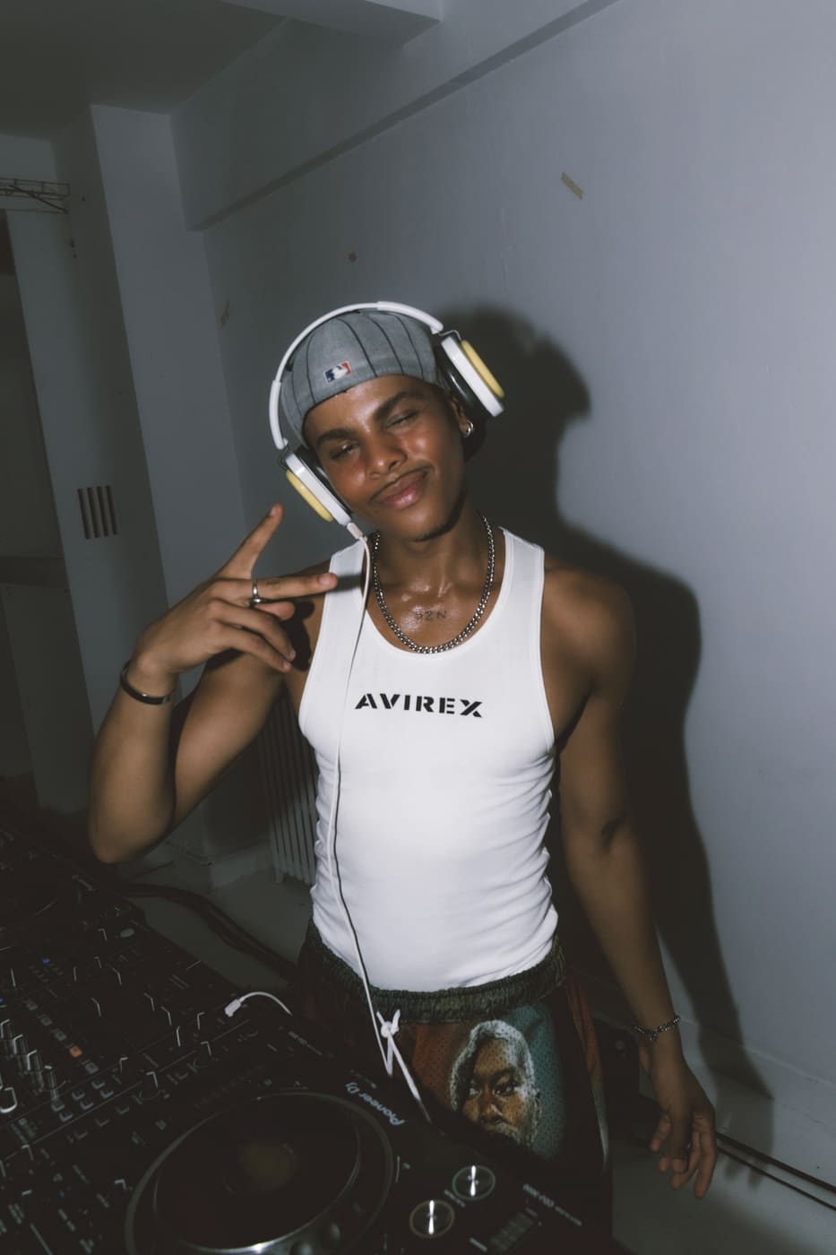 Oluwa at the decks in headphones, two fingers raised to the camera