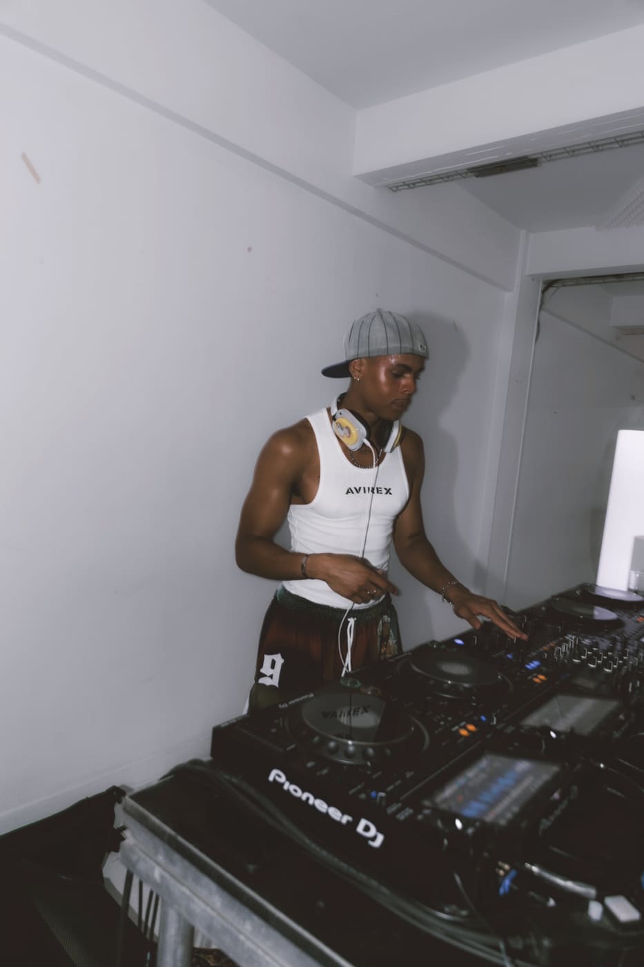Oluwa alone at the decks, cap turned backwards, one hand reaching across the mixer