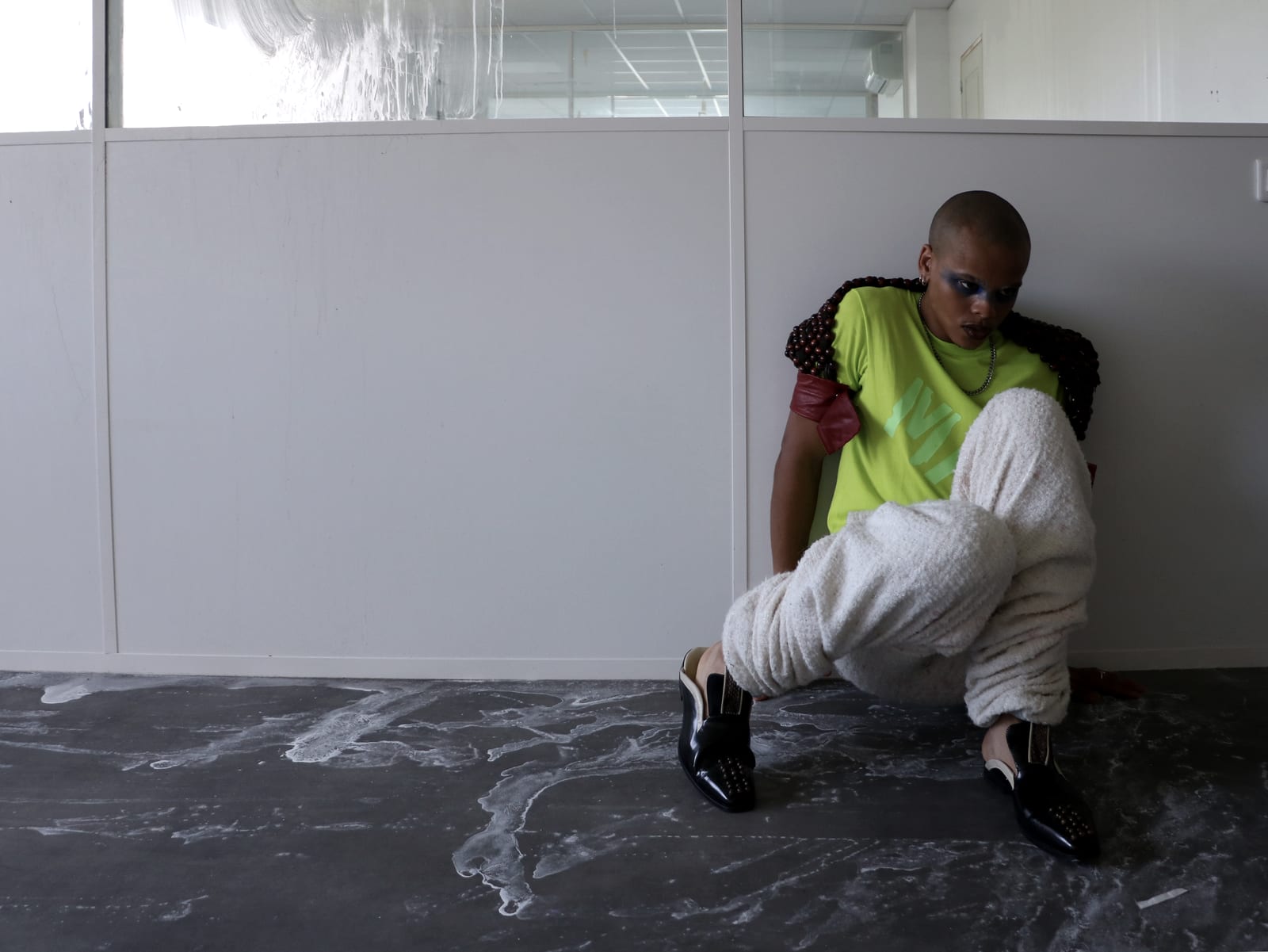 Oluwa seated against the wall in fleece trousers, one knee up