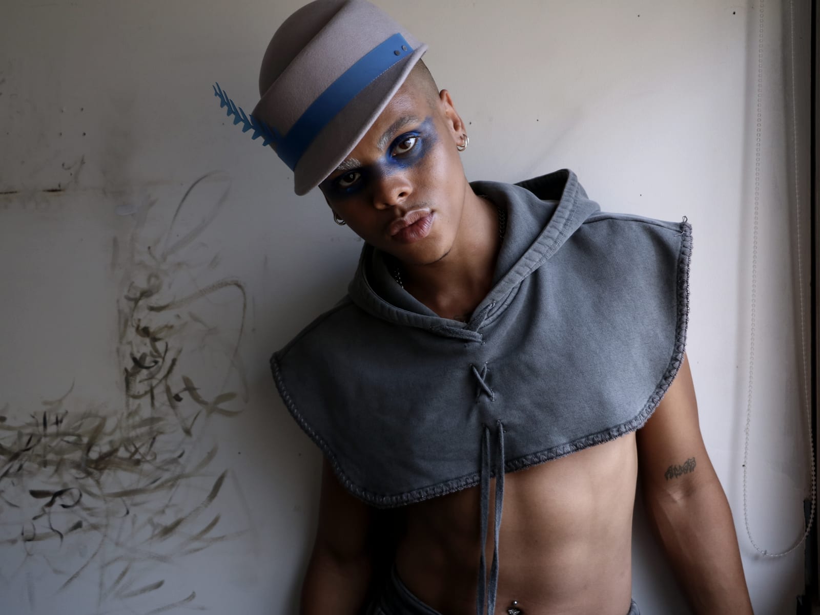 Oluwa in the felt hat, chin lifted, eyes shaded blue